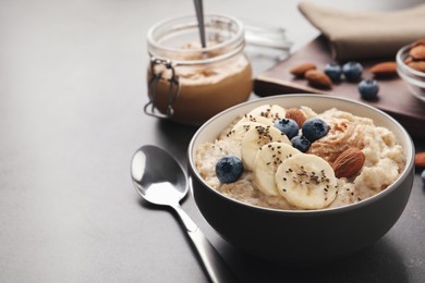 Photo of Tasty oatmeal porridge with toppings served on grey table, space for text