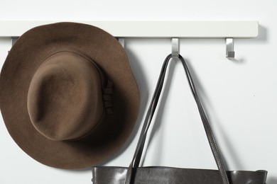 Photo of Brown hat and bag hanging on hook rack on white wall