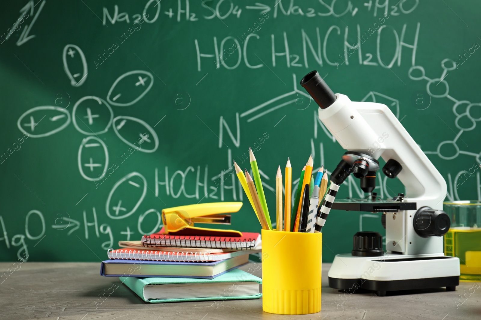 Photo of Laboratory glassware, microscope and stationery on table near chalkboard. Chemistry concept