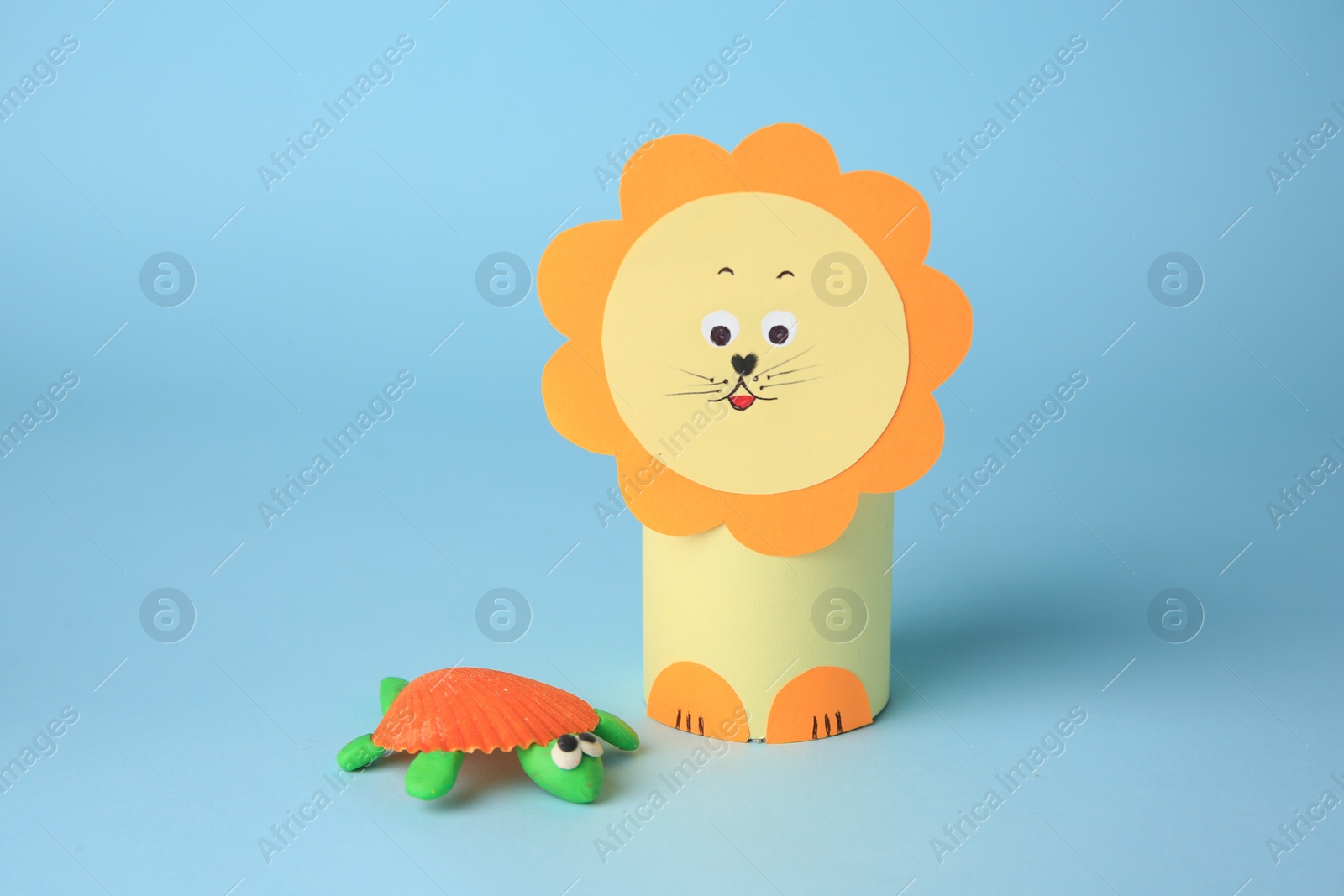 Photo of Toy lion made from toilet paper hub and plasticine turtle on light blue background. Children's handmade ideas