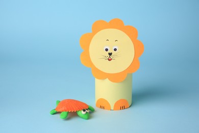 Photo of Toy lion made from toilet paper hub and plasticine turtle on light blue background. Children's handmade ideas