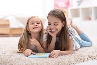 Cute little sisters reading book together at home