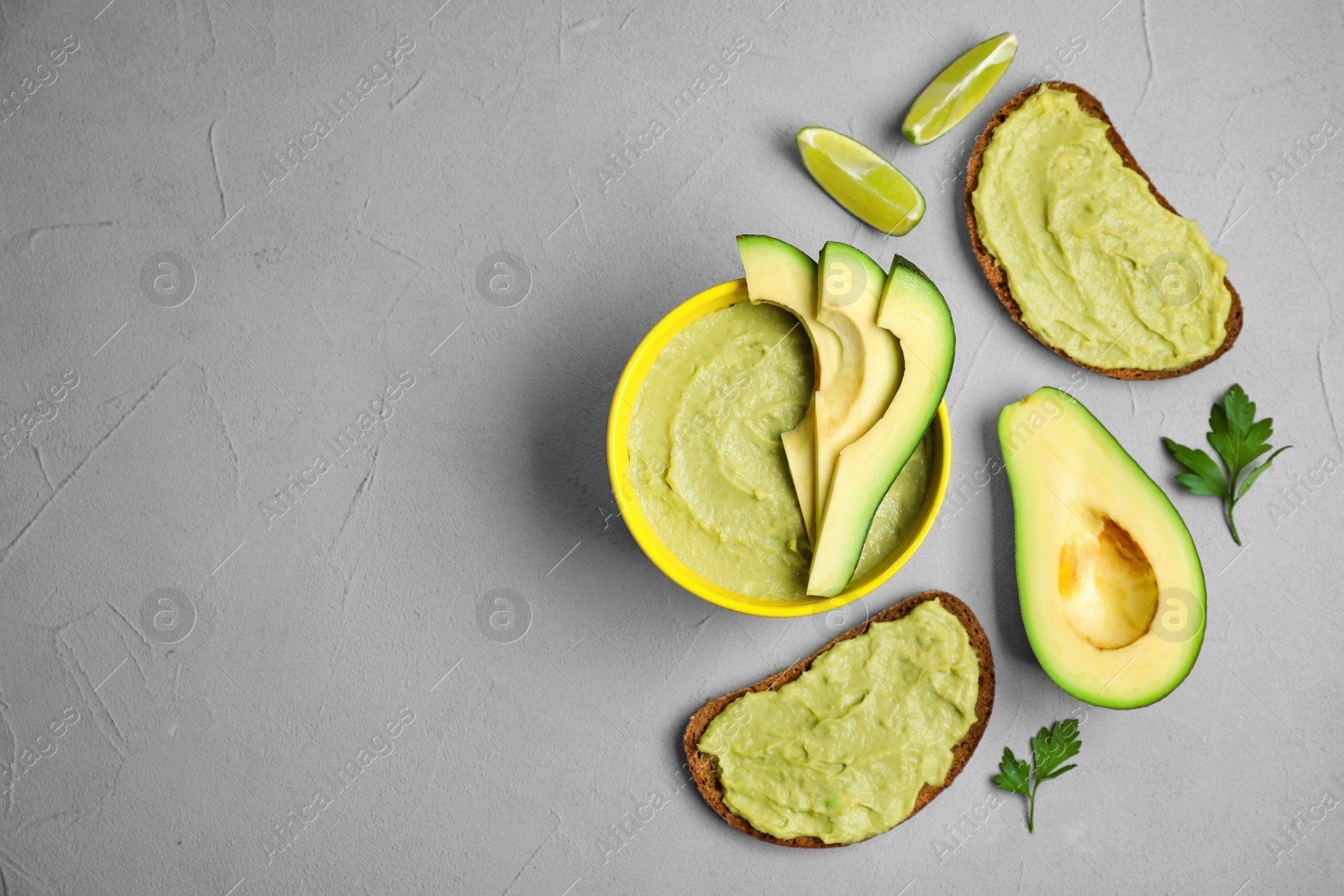 Photo of Flat lay composition with bowl of guacamole made of ripe avocados on grey table. Space for text