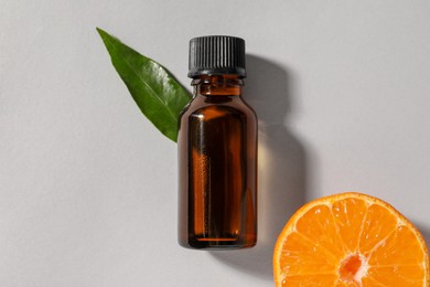Photo of Aromatic tangerine essential oil in bottle, leaf and citrus fruit on grey table, top view