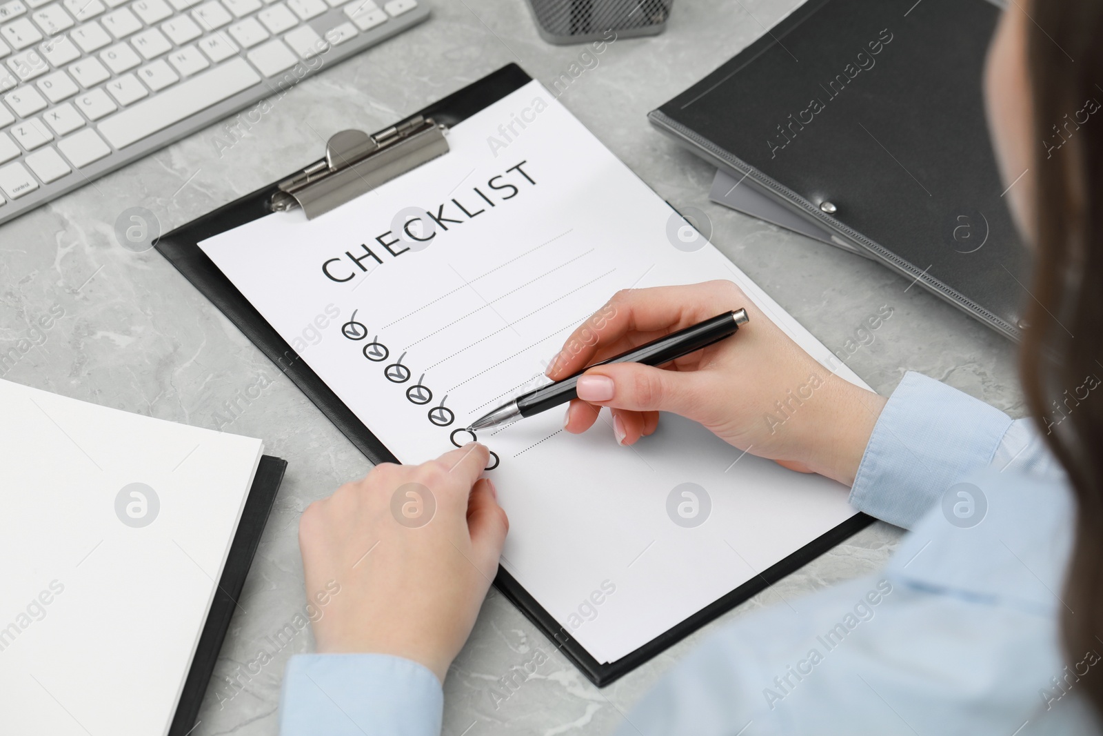 Photo of Woman filling Checklist at grey marble table, closeup