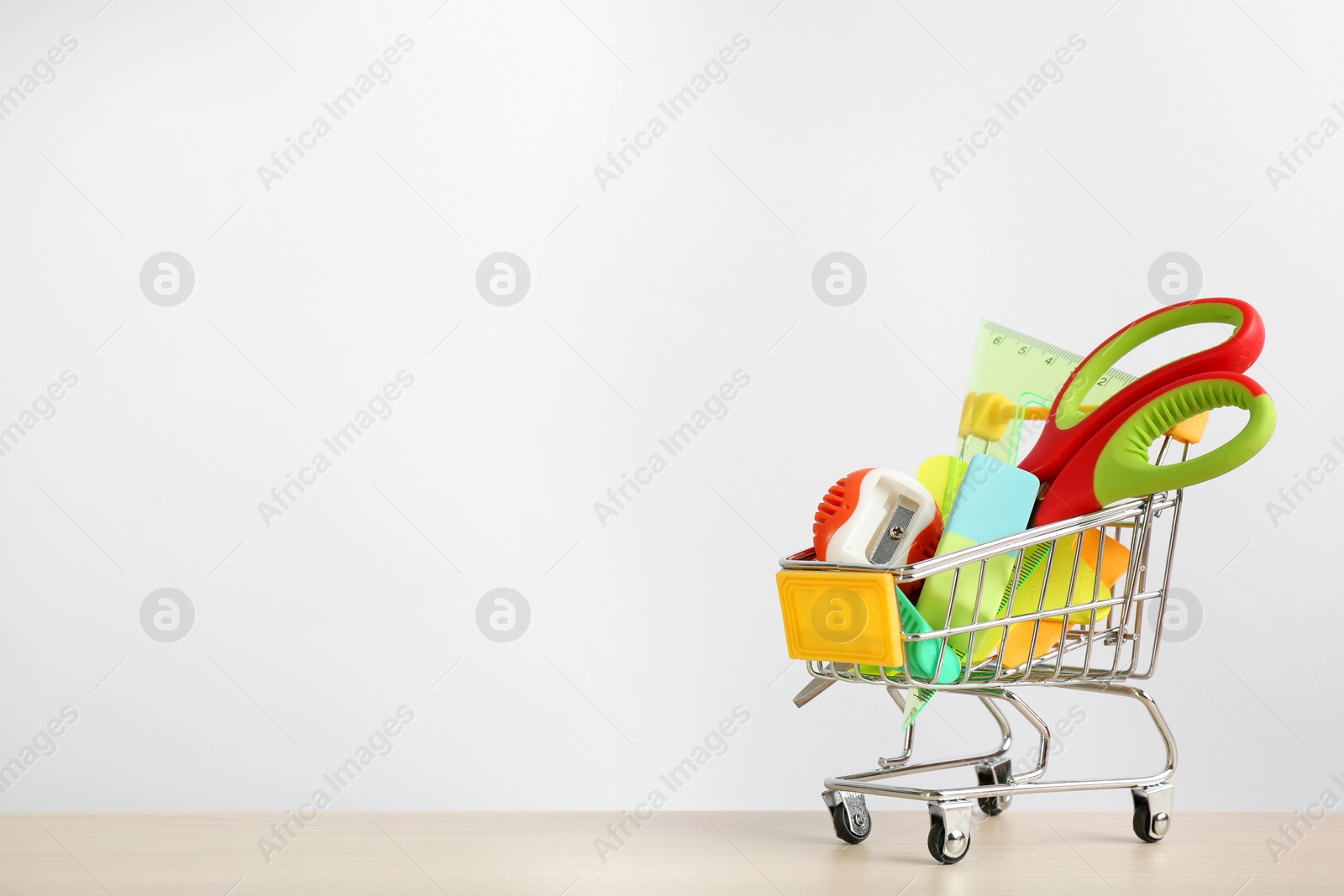 Photo of Different school stationery in miniature shopping cart on table against white background, space for text. Back to school