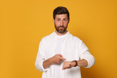 Photo of Bearded man pointing at wristwatch on orange background