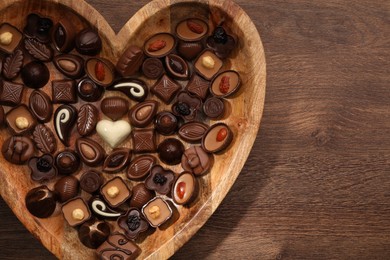 Heart shaped plate with delicious chocolate candies on wooden table, top view