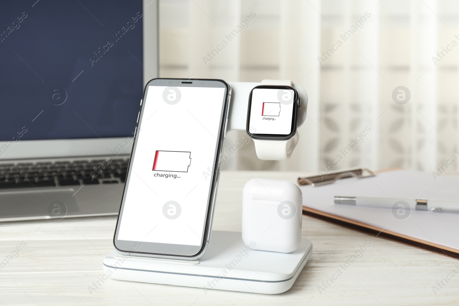 Photo of Set of gadgets charging with wireless device on white wooden table