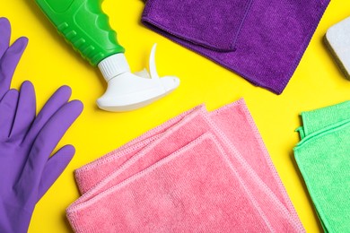 Microfiber cloths and cleaning supplies on yellow background, flat lay