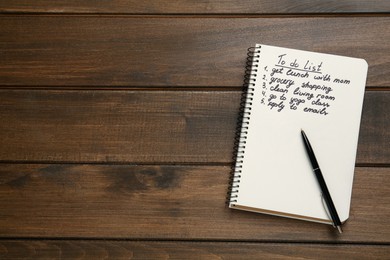 Notebook with to do list and pen on wooden table, flat lay. Space for text