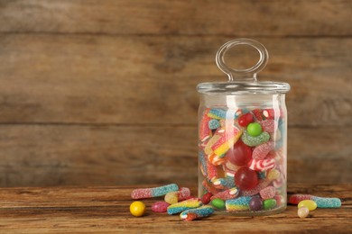 Photo of Jar with different delicious candies on wooden table, space for text