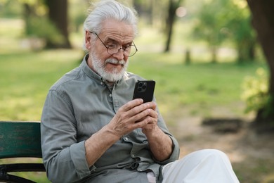 Portrait of happy grandpa with glasses using smartphone on bench in park