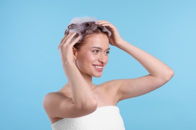 Happy young woman washing her hair with shampoo on light blue background