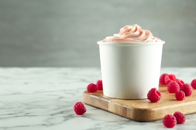 Cup with tasty frozen yogurt and raspberries on marble table. Space for text