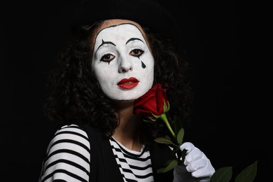 Photo of Young woman in mime costume with red rose posing on black background
