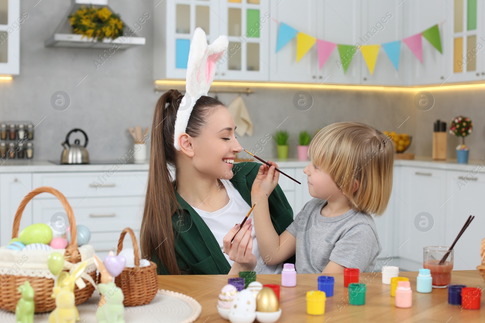 Photo of Mother and her son having fun while painting Easter eggs at table in kitchen