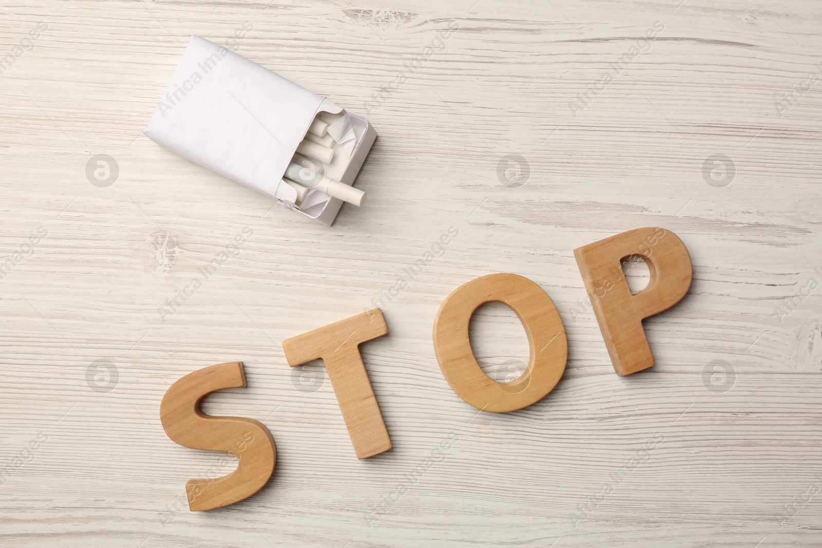 Photo of Pack with cigarettes and word Stop made of letters on white wooden table, flat lay. No smoking concept