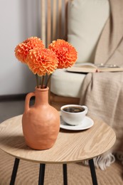 Photo of Ceramic vase with beautiful flowers on coffee table near armchair indoors