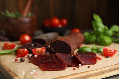 Photo of Delicious dry-cured beef basturma with basil, tomatoes and spices on wooden table, closeup