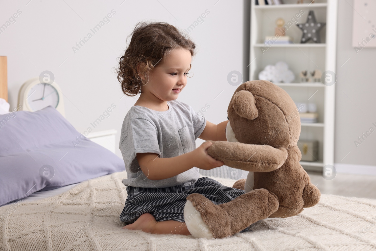 Photo of Cute little girl playing with teddy bear on bed at home