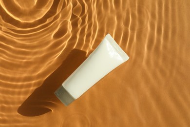Tube with moisturizing cream in water on orange background, top view