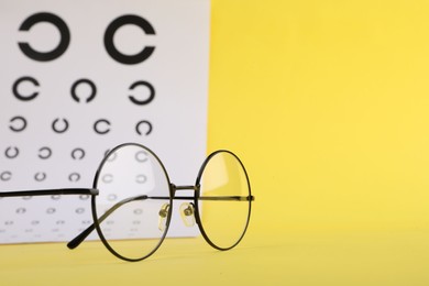 Photo of Vision test chart and glasses on yellow background, closeup. Space for text