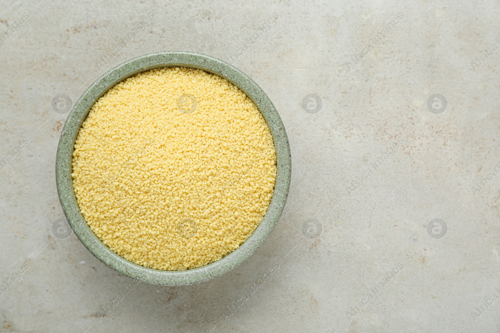 Photo of Bowl of raw couscous on light table, top view. Space for text