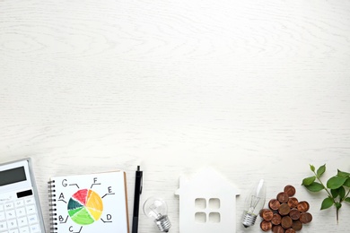 Flat lay composition with energy efficiency rating chart, house figure and coins on white wooden background. Space for text