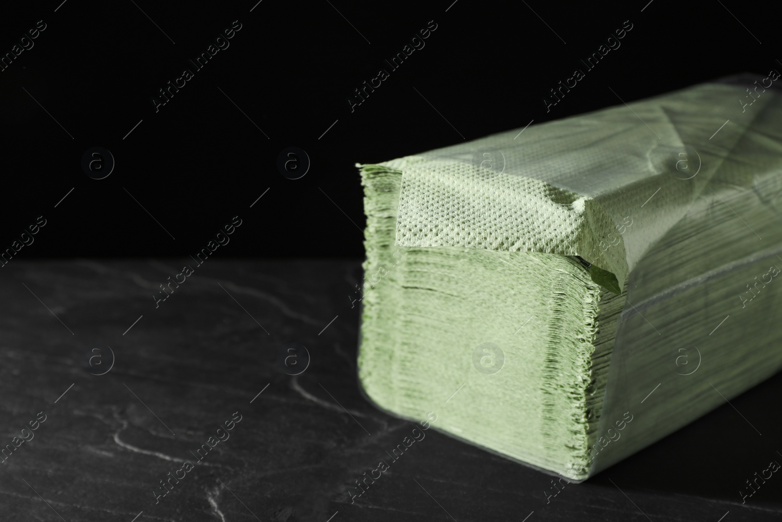Photo of Stack of green paper napkins on grey table against black background. Space for text