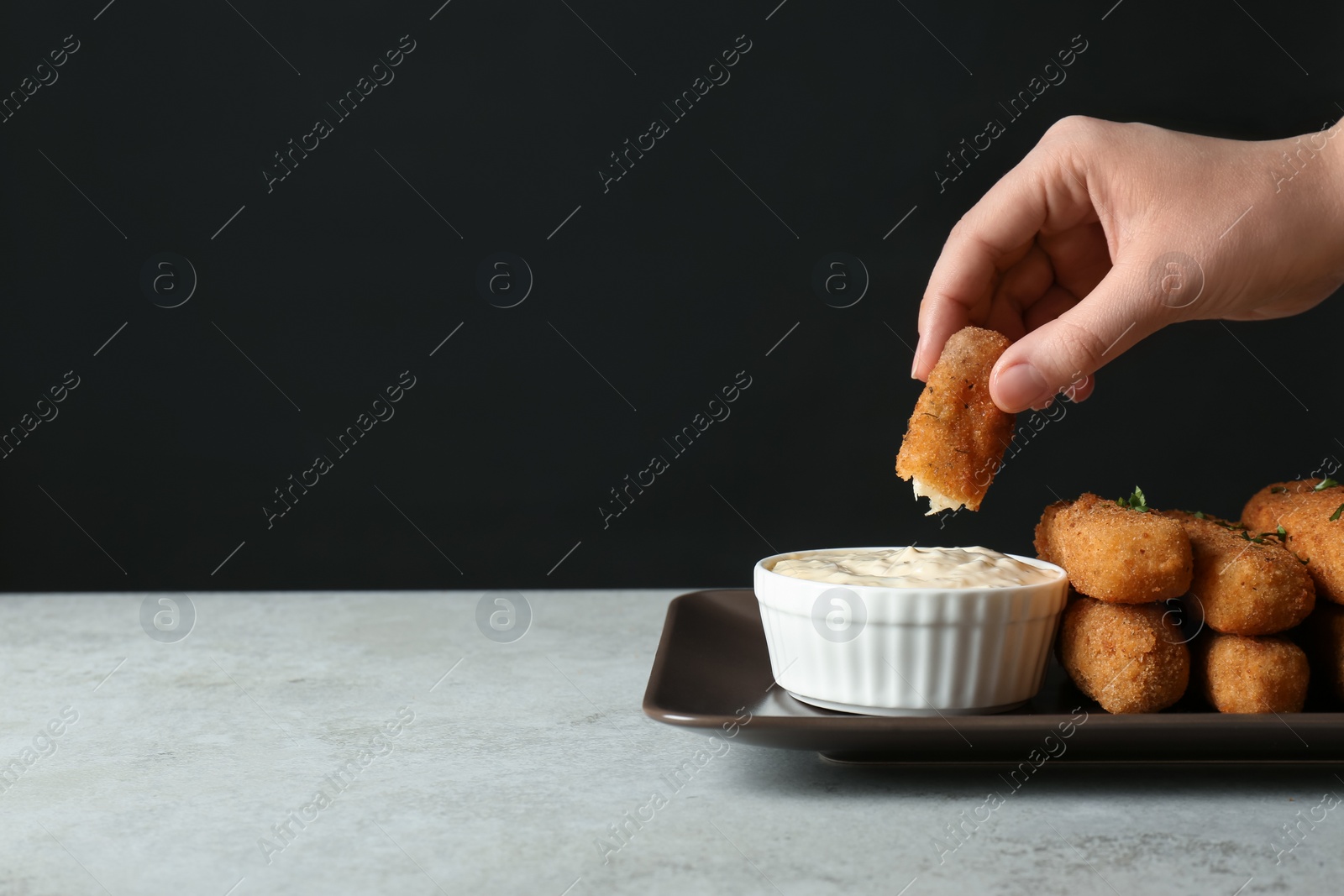 Photo of Woman dipping cheese stick into sauce at table, closeup. Space for text