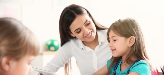 Image of Teacher helping girl with her task in classroom at school. Banner design
