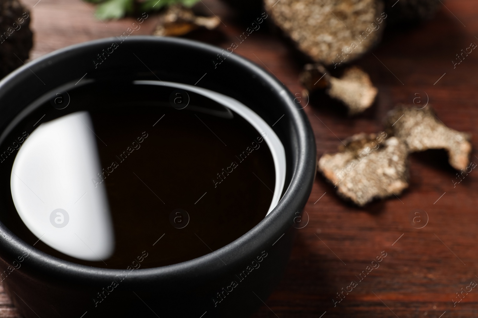 Photo of Fresh truffle oil in bowl on wooden table, closeup