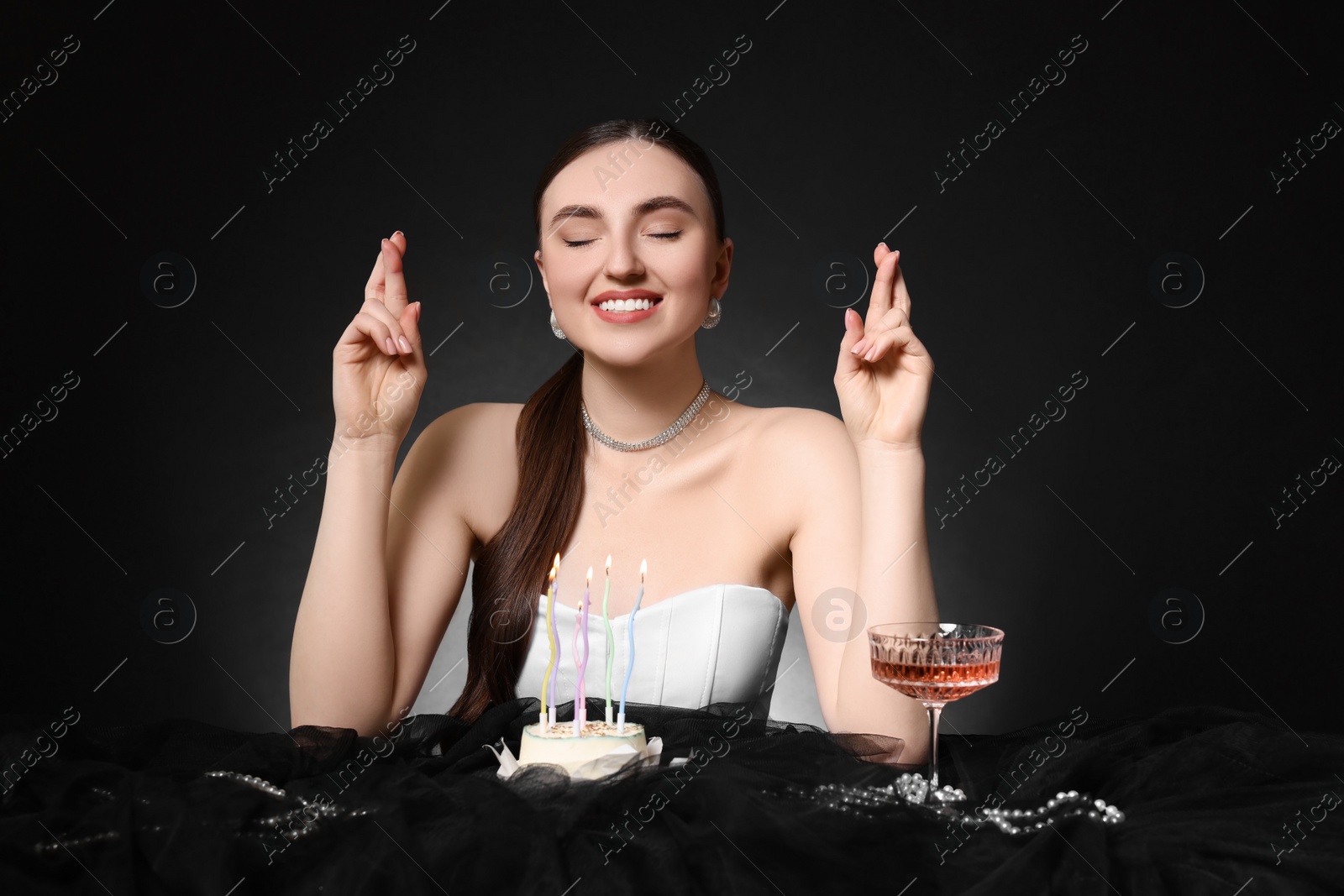 Photo of Fashionable photo of attractive young woman making wish with her Birthday cake on black background