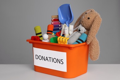 Donation box with different toys on white table against grey background