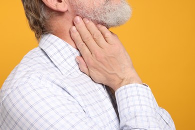 Photo of Senior man suffering from sore throat on yellow background, closeup. Cold symptoms