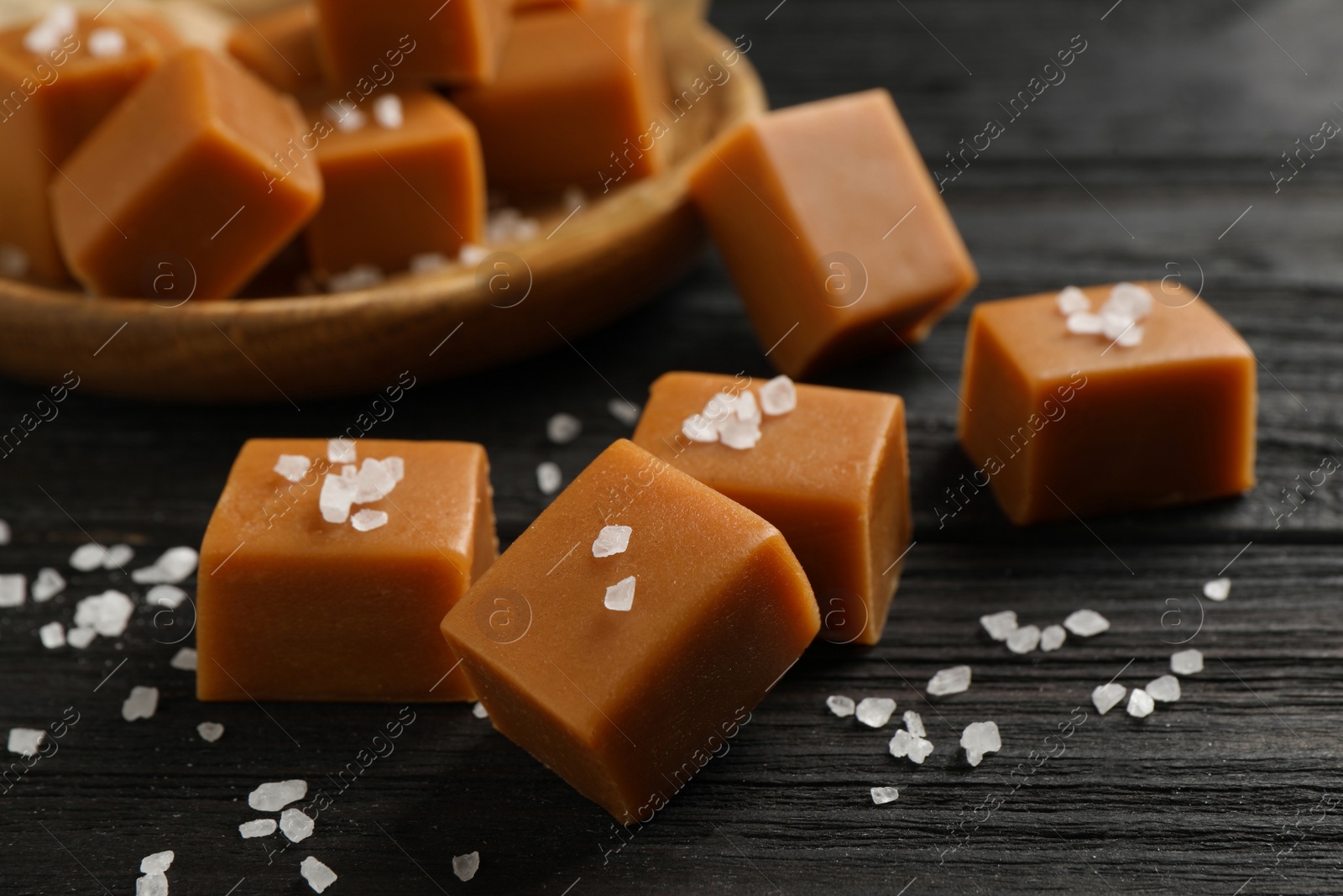 Photo of Yummy caramel candies and sea salt on black wooden table, closeup