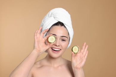 Photo of Woman with towel holding pieces of cucumber on beige background. Spa treatment