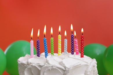 Photo of Delicious cake with burning candles and festive decor on red background, closeup