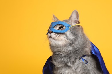 Adorable cat in blue superhero cape and mask on yellow background, space for text