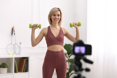 Smiling sports blogger working out with dumbbells while recording fitness lesson at home