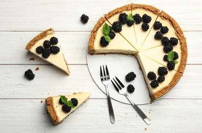 Photo of Sliced delicious cheesecake with blackberries on white wooden background, flat lay