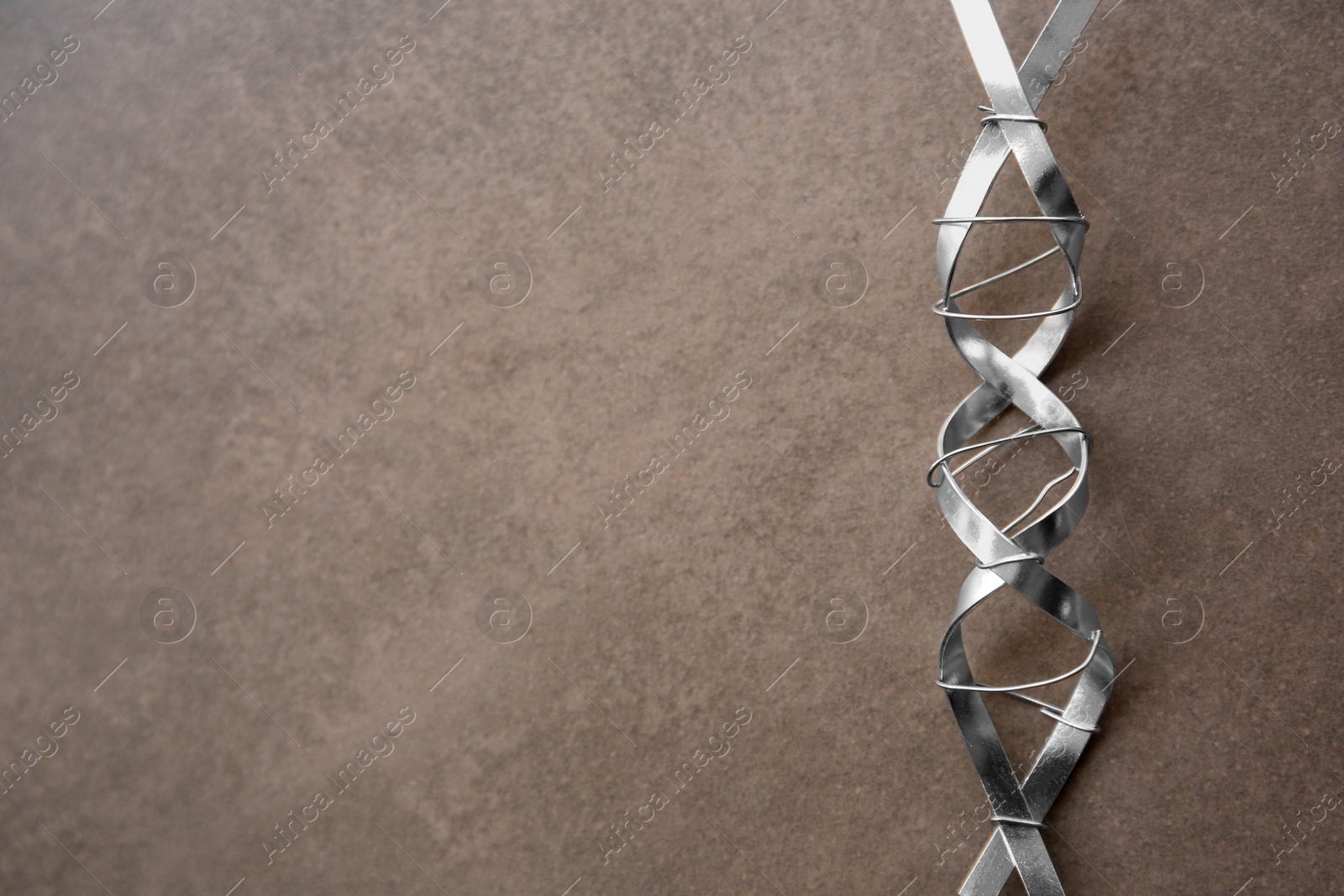 Photo of DNA molecule model made of metal on brown background, top view. Space for text