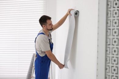 Man hanging stylish gray wallpaper in room