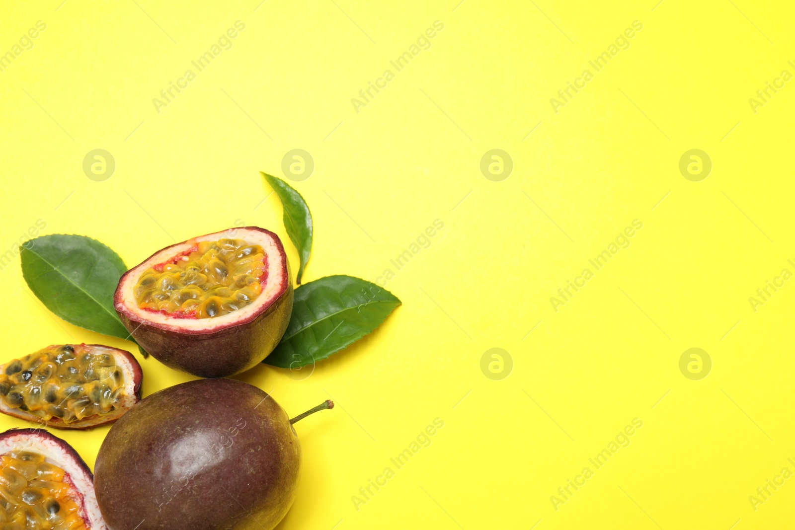 Photo of Fresh ripe passion fruits (maracuyas) with green leaves on yellow background, flat lay. Space for text