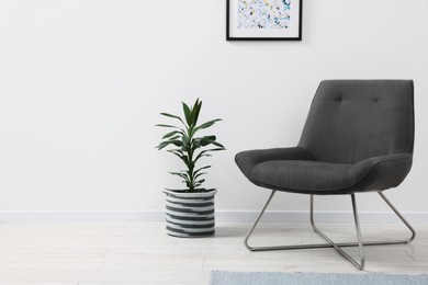 Photo of Comfortable armchair and houseplant near white wall indoors, space for text. Interior design