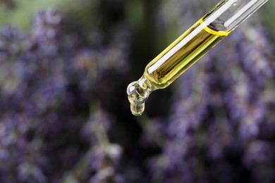 Photo of Dripping lavender essential oil from pipette against blurred background, closeup. Space for text