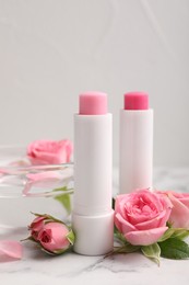 Photo of Lip balms, bowl with water and roses on white marble table