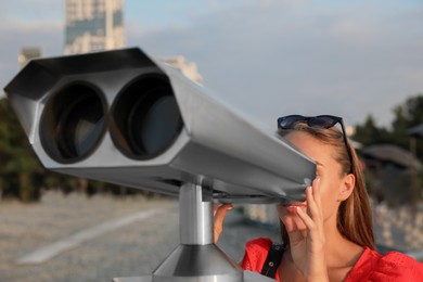 Photo of Young woman looking through tourist viewing machine at observation deck