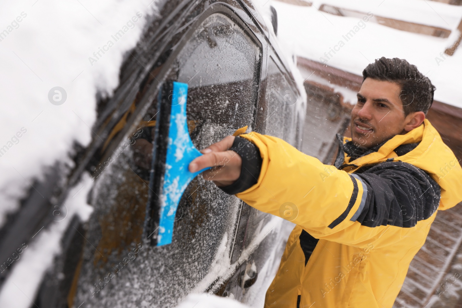 Photo of Man cleaning snow from car window outdoors on winter day